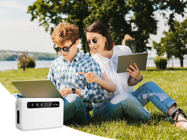 A young couple using a laptop and tablet in a park, connected to the internet with a portable Wi-Fi router.